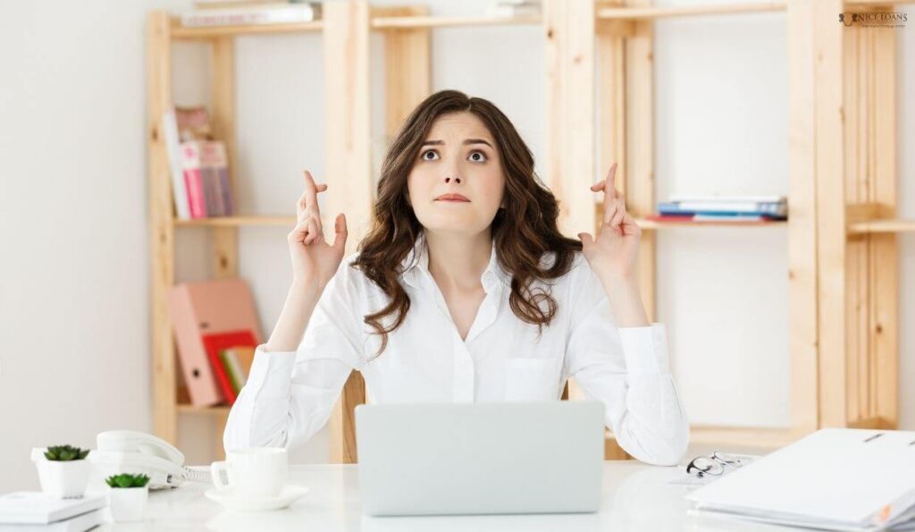 A young lady at her desk with her fingers crossed. 