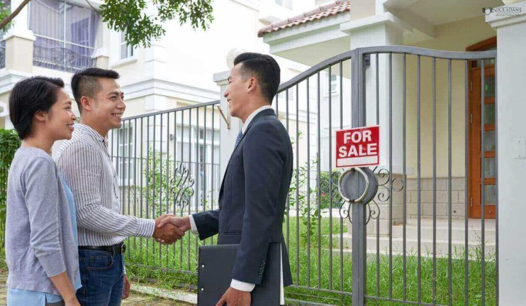 A man in a suit before a home that says for sale shaking hands with a couple.
