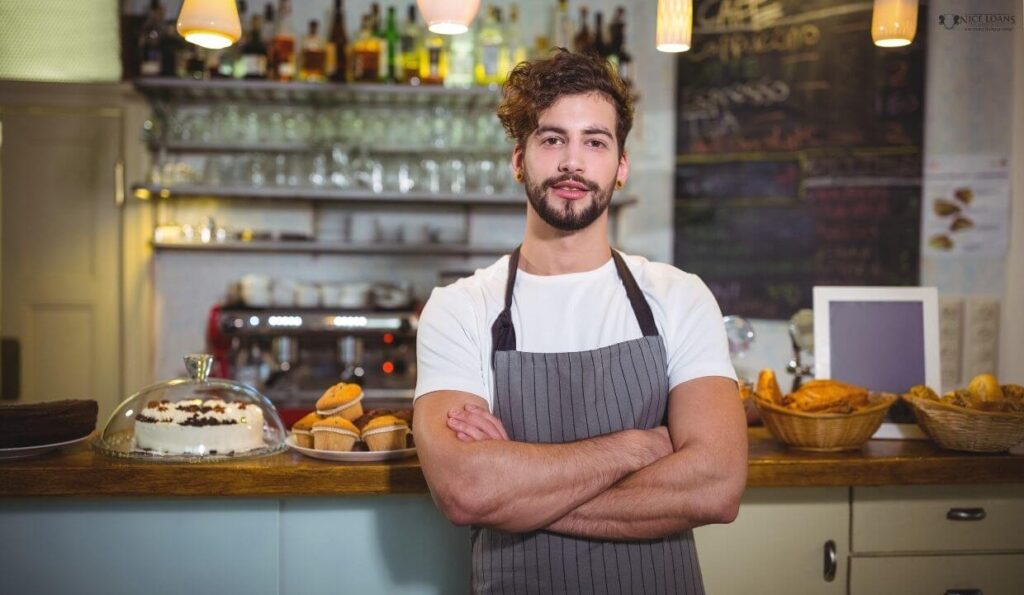 a self employed barista posing before a counter with his hands folded. 