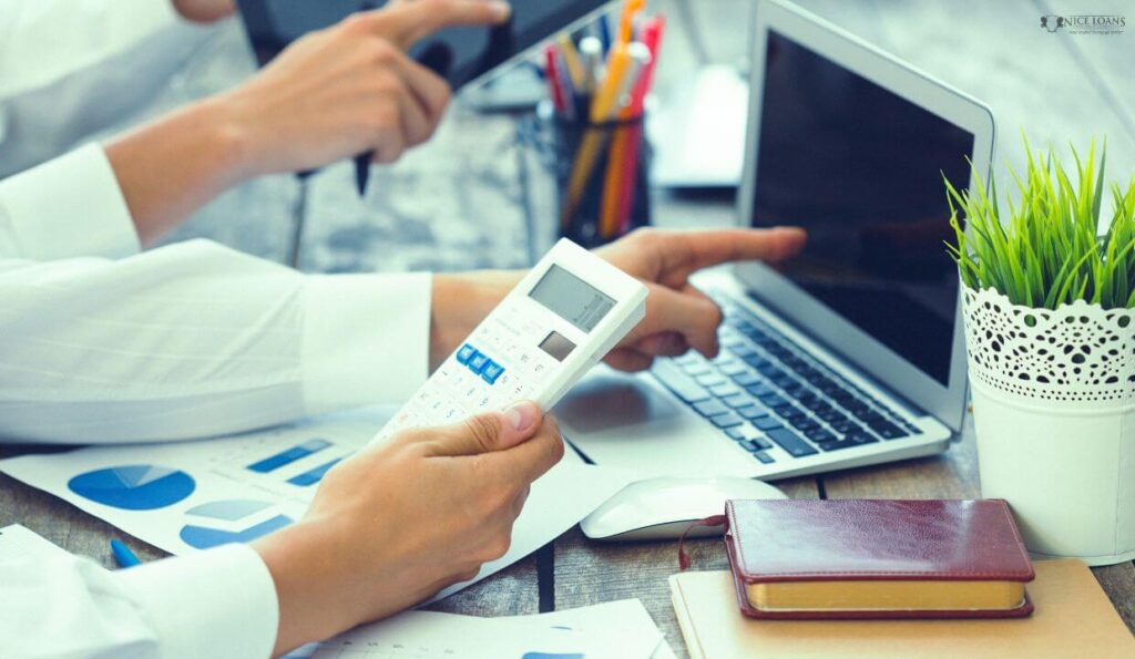 a closeup of hands working on a laptop with a calculator in another.