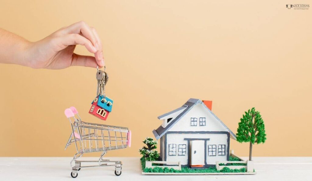 a mini shopping cart and a mini model home on a table with a hand holding down home keys. 
