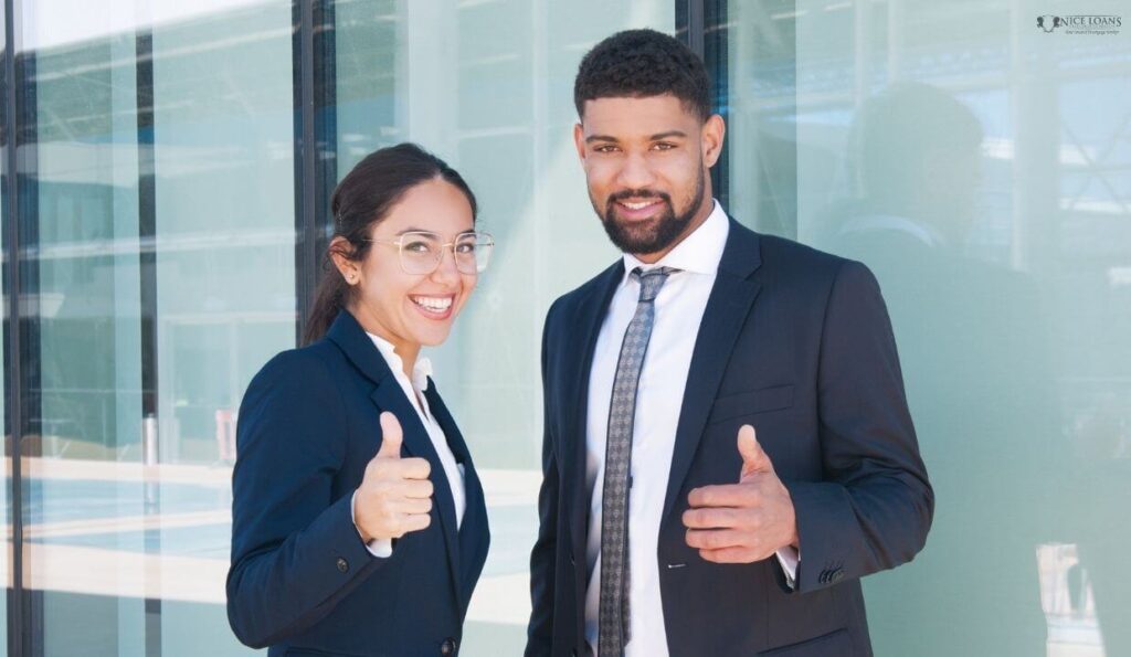 Two business partners smiling at the camera, posing with a thumbs up. 