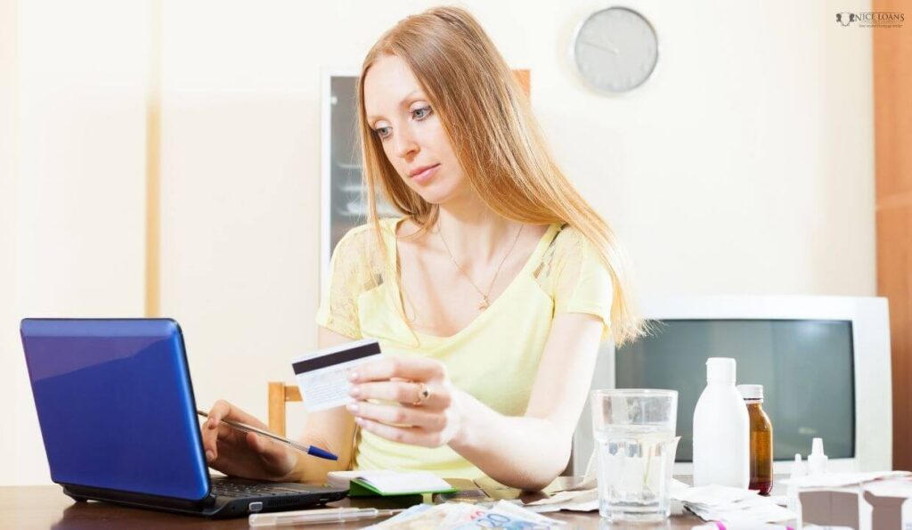 woman looking at her credit card and laptop, looking pensive.

