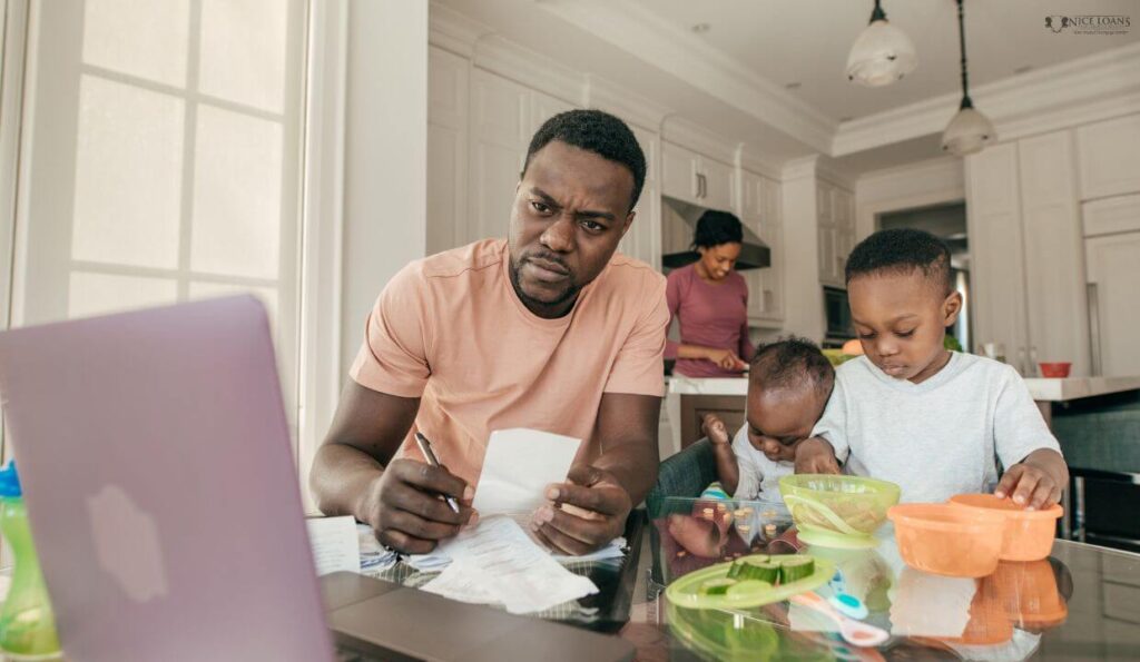 a family of four in their kitchen with the mother working at the counter, while the father is working on his home loan papers with the kids beside him at the coffee table.