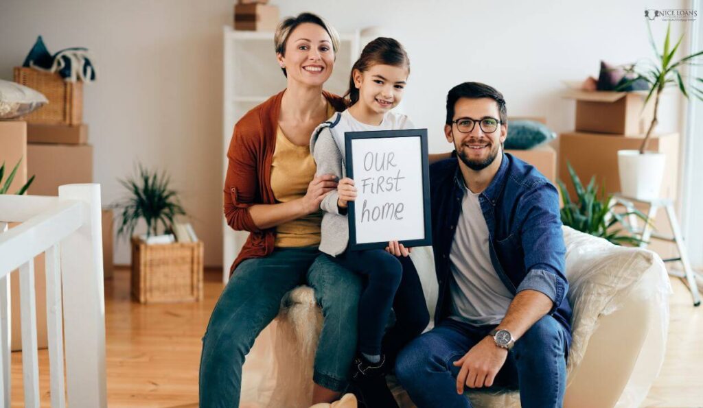 A happy family of three in their first home, with the kid holding a frame that says our first home.
