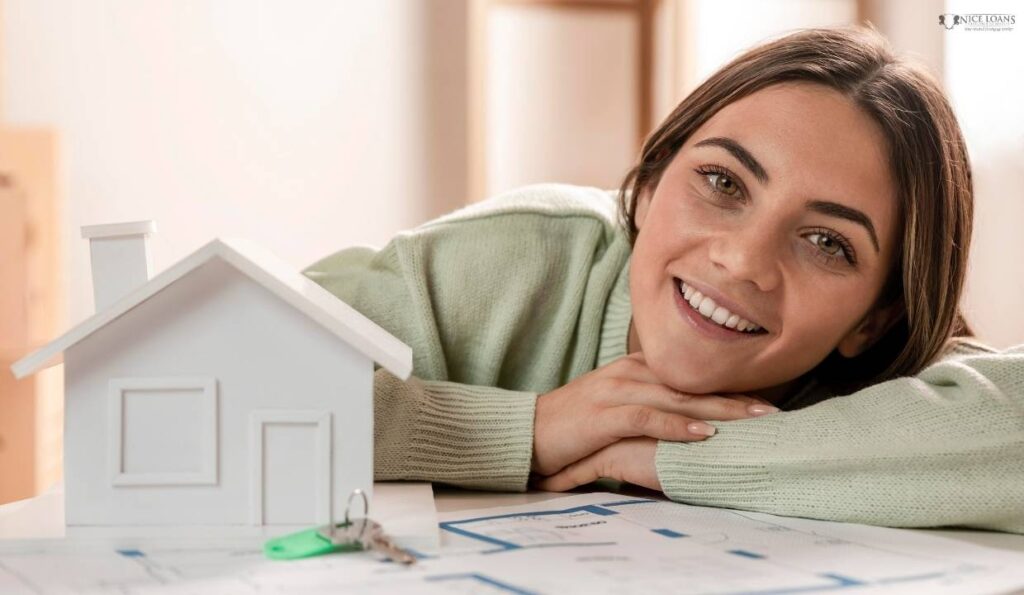 A medium shot of a woman at a table with her head resting on her hands beside a model house. 