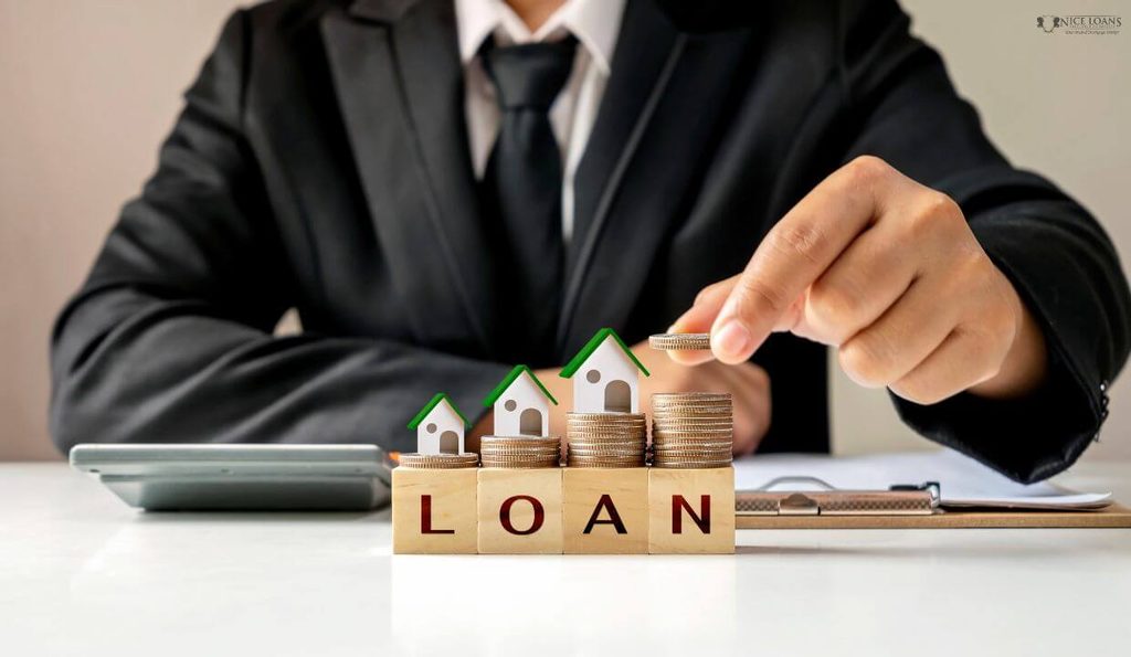 A mortgage broker stacking coins and little model houses over blocks with loan written on it.